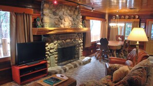 A cozy living room with a stone fireplace, a flat-screen TV, a comfortable sofa, and a dining area with a table and chairs. - Half Dome (Yosemite National Park)