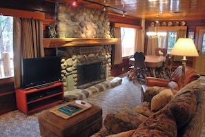 A cozy living room with a stone fireplace, a flat-screen TV on a wooden stand, a comfortable sofa, and a dining area with a table and chairs. - Half Dome (Yosemite National Park)