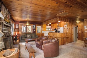 L’intérieur chaleureux d’un chalet avec des murs en bois, une cheminée, un canapé, une table basse et un coin cuisine.