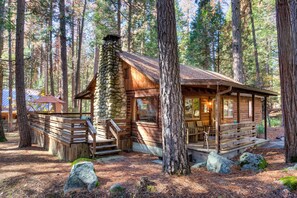 Un chalet rustique doté d’une cheminée en pierre, d’une terrasse en bois et d’un porche aménagé avec des sièges.