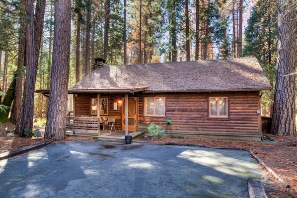 Une cabane en bois dotée d’un porche, entourée de grands arbres.