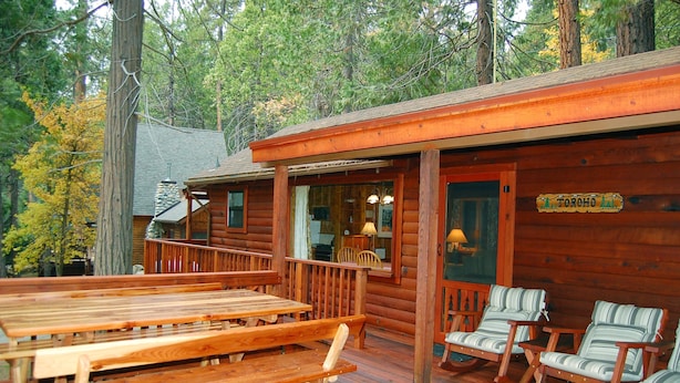 Eine Holzhütte mit Veranda, Picknicktischen und gestreiften Stühlen.