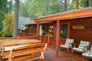 Una cabaña de madera con un porche, mesas de picnic y sillas a rayas.