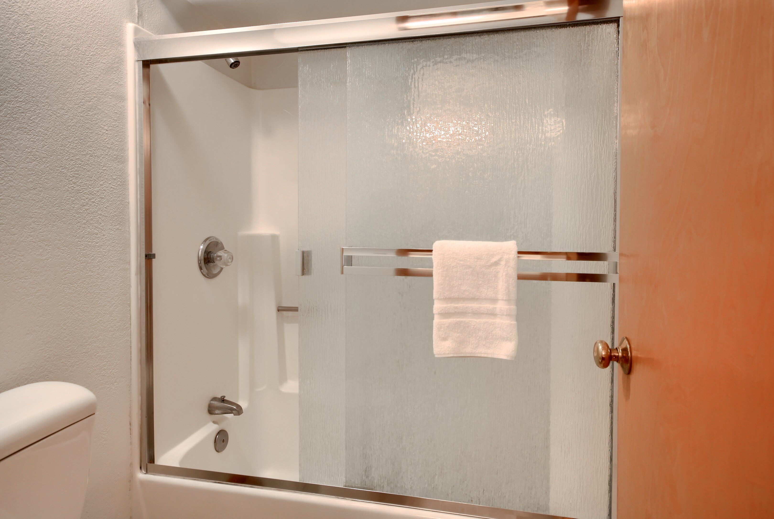 Et brusebad med glasvægge, et håndklædetørrestativ og et synligt toilet.