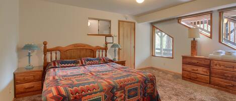 A bedroom with a large bed, wooden headboard, two bedside tables with lamps, a dresser, and a window with a view of trees.