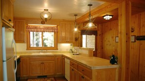 A wooden kitchen with a refrigerator, sink, and wooden cabinets. There are two pendant lights above the counter. - 9N Fox Hollow (Yosemite National Park)