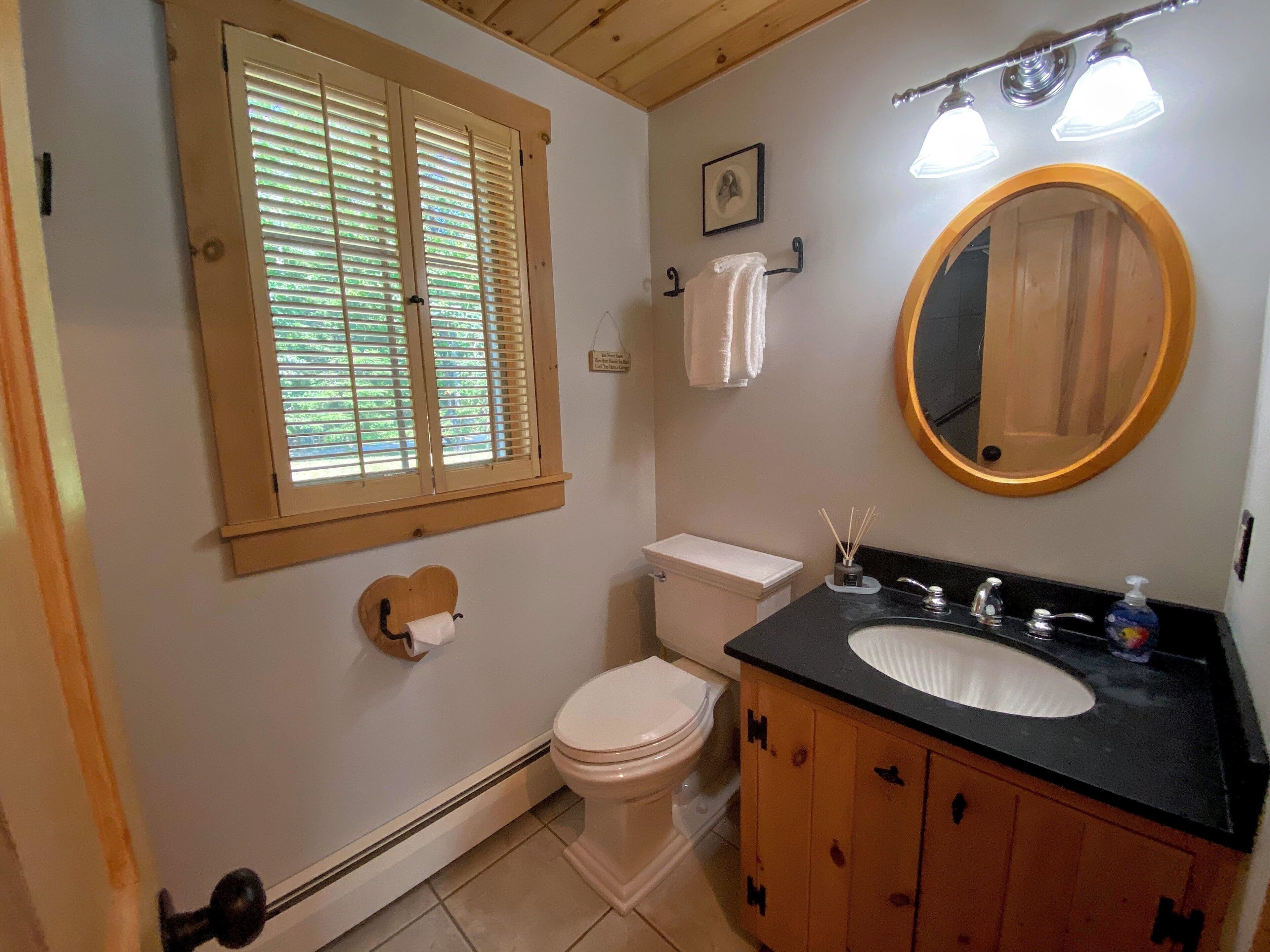 Un baño con inodoro, lavamanos, tocador, espejo, toallero y ventana con persianas.