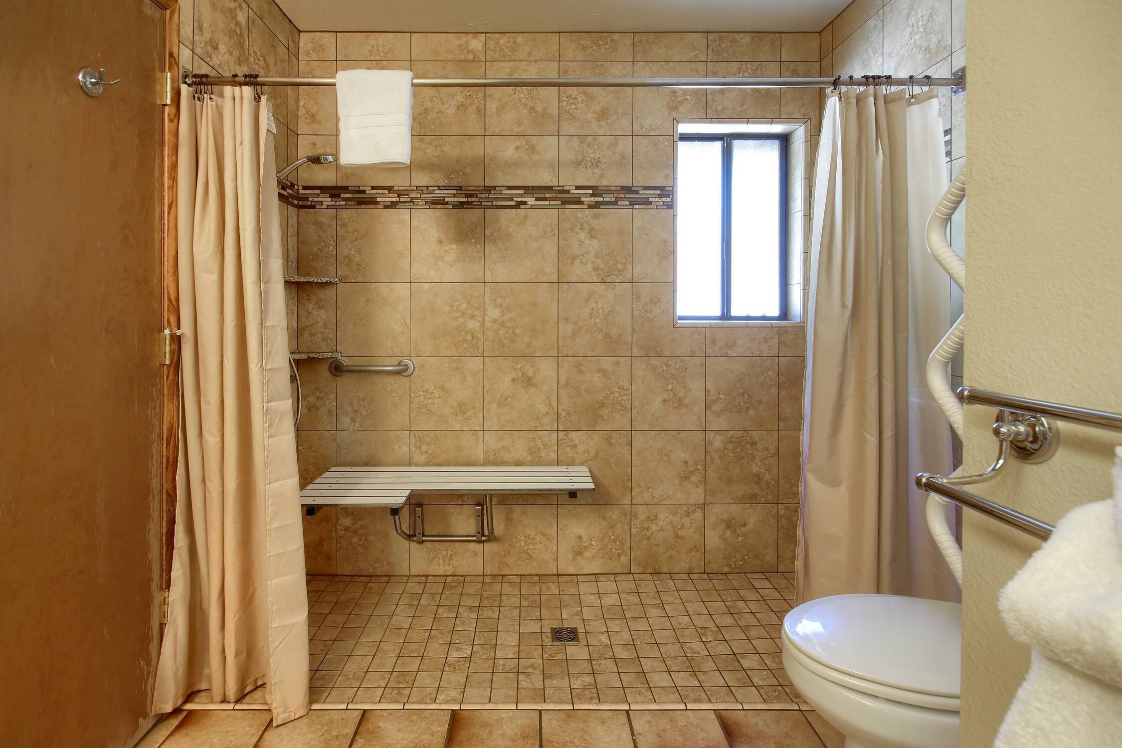 Un espace douche équipé d’un banc, d’une fenêtre et de toilettes.
