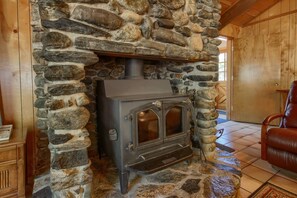 A stone fireplace with a wood-burning stove, a leather chair, and a wooden cabinet. - Bordentown West (Yosemite National Park)