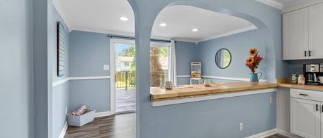A kitchen with light blue walls, wooden flooring, and white cabinets.