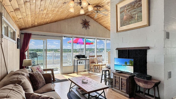 Un soggiorno spazioso con un divano grande, un tavolino in legno e una televisione su un mobile. Include un balcone con vista sulla città e un ombrello colorato.