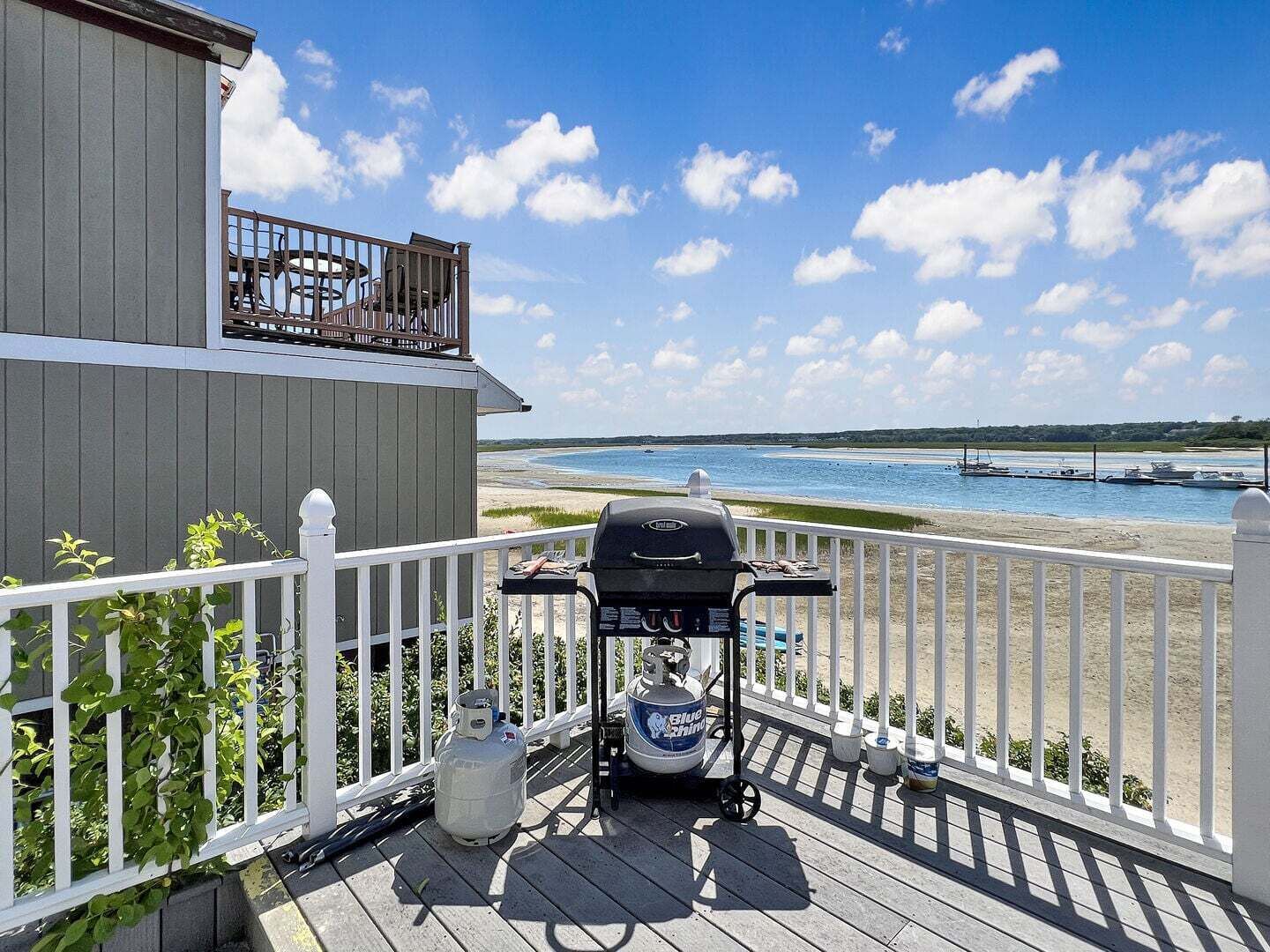 A deck with a grill, propane tank, and a view of the beach and water.