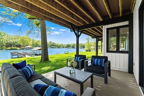 A covered outdoor seating area with a view of a lake, a dock, and a grassy lawn. - Fox Run LKN (Denver)