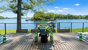Een houten terras met een tafel voor twee, met uitzicht op een meer met boten en een gazebo.