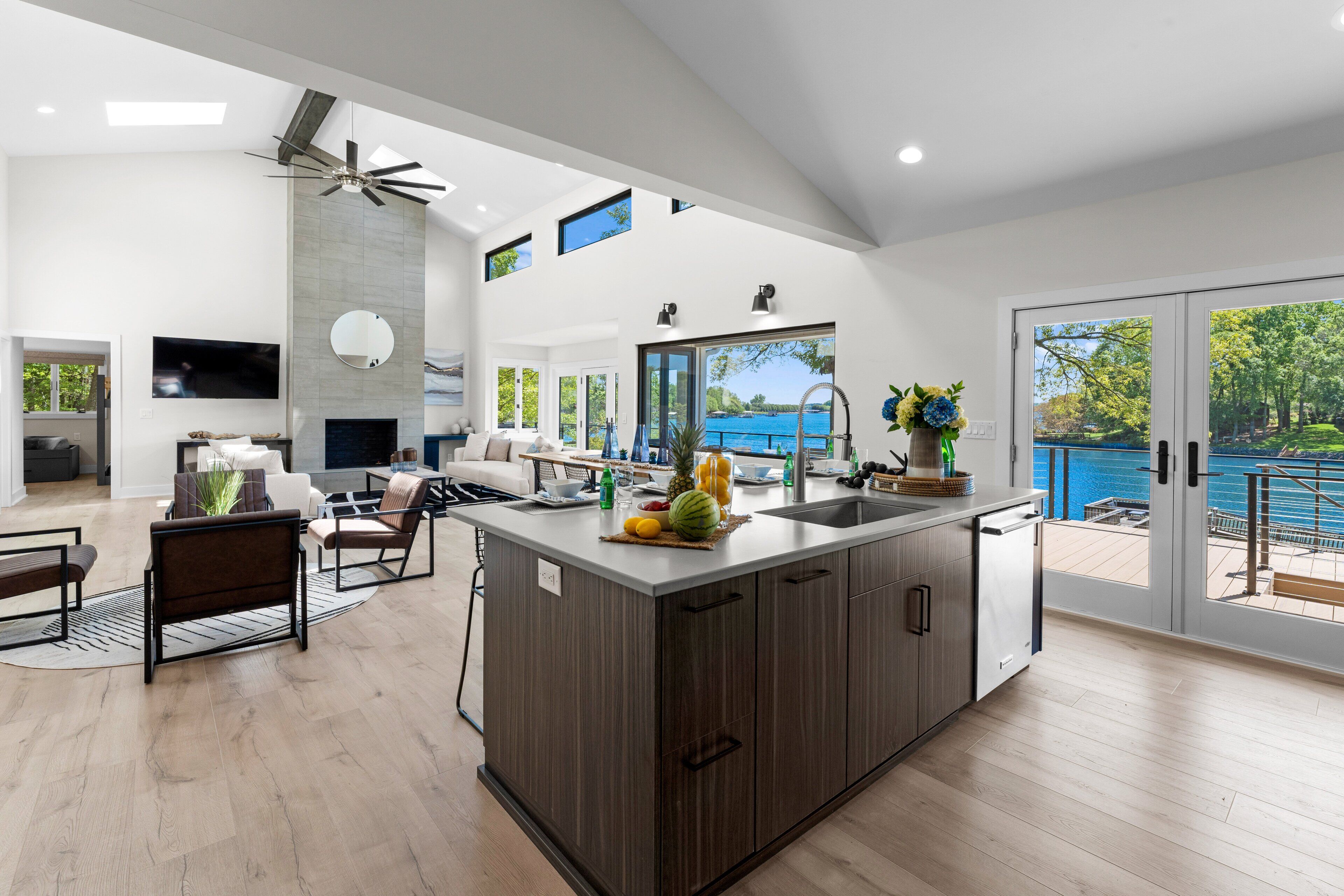 A modern kitchen with a large island, a dining area with a sofa, and a view of a blue body of water through large sliding doors.