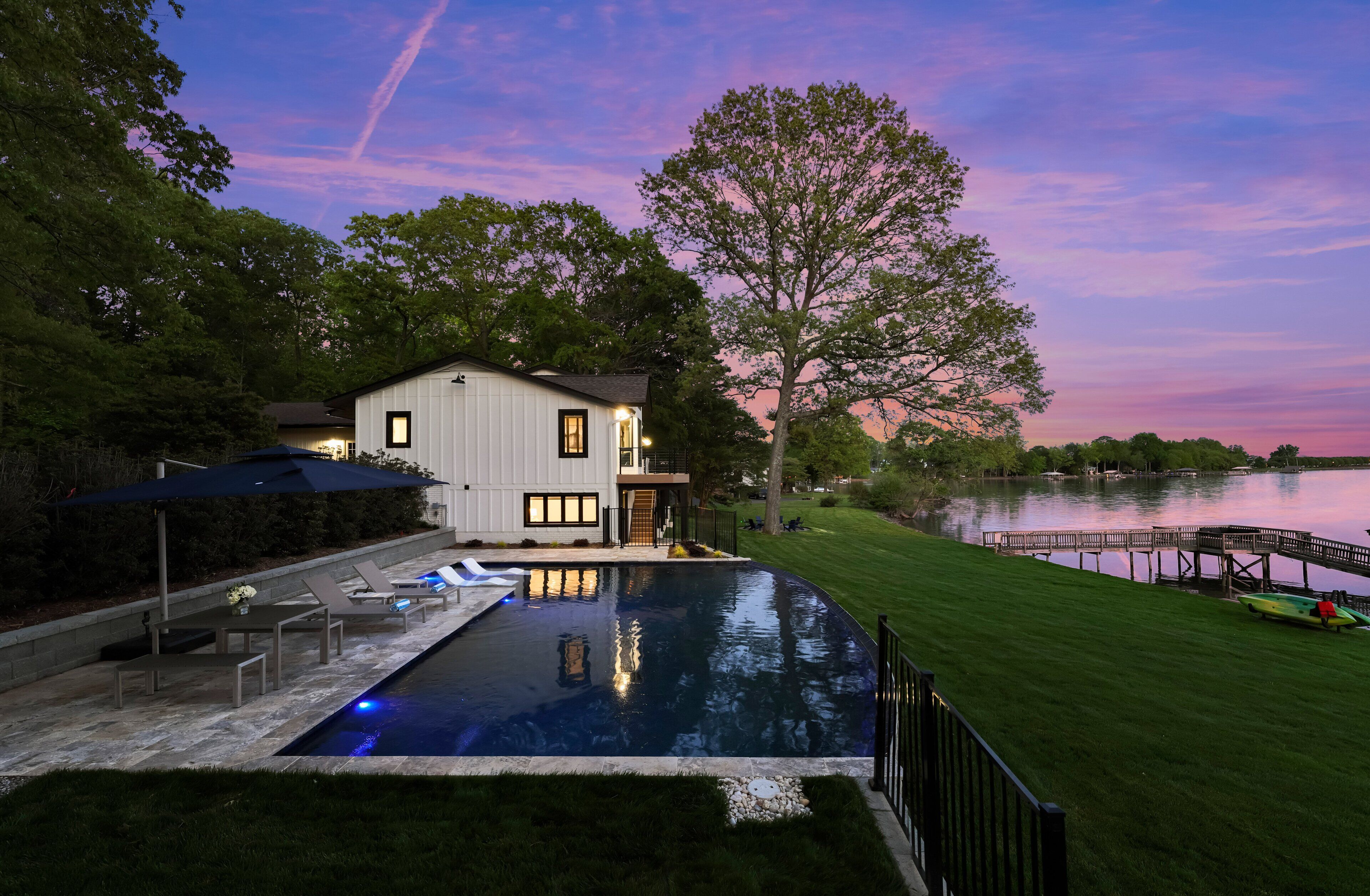 Une maison moderne avec une piscine, entourée d’une pelouse bien entretenue et d’un quai au bord d’un lac.
