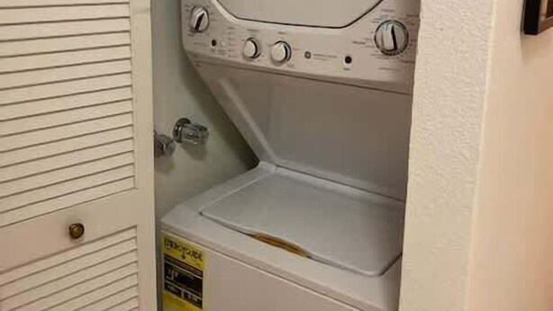 Une petite buanderie blanche, dotée d’un lave-linge et d’un sèche-linge encastrés, d’une petite étagère et d’une porte avec une poignée.