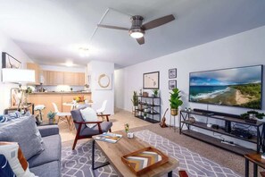 A modern living room with a grey sofa, wooden coffee table, and a large flat-screen TV mounted on the wall. - Beachfront Bliss Walk to Sand, Pool, Restaurants (Kihei)