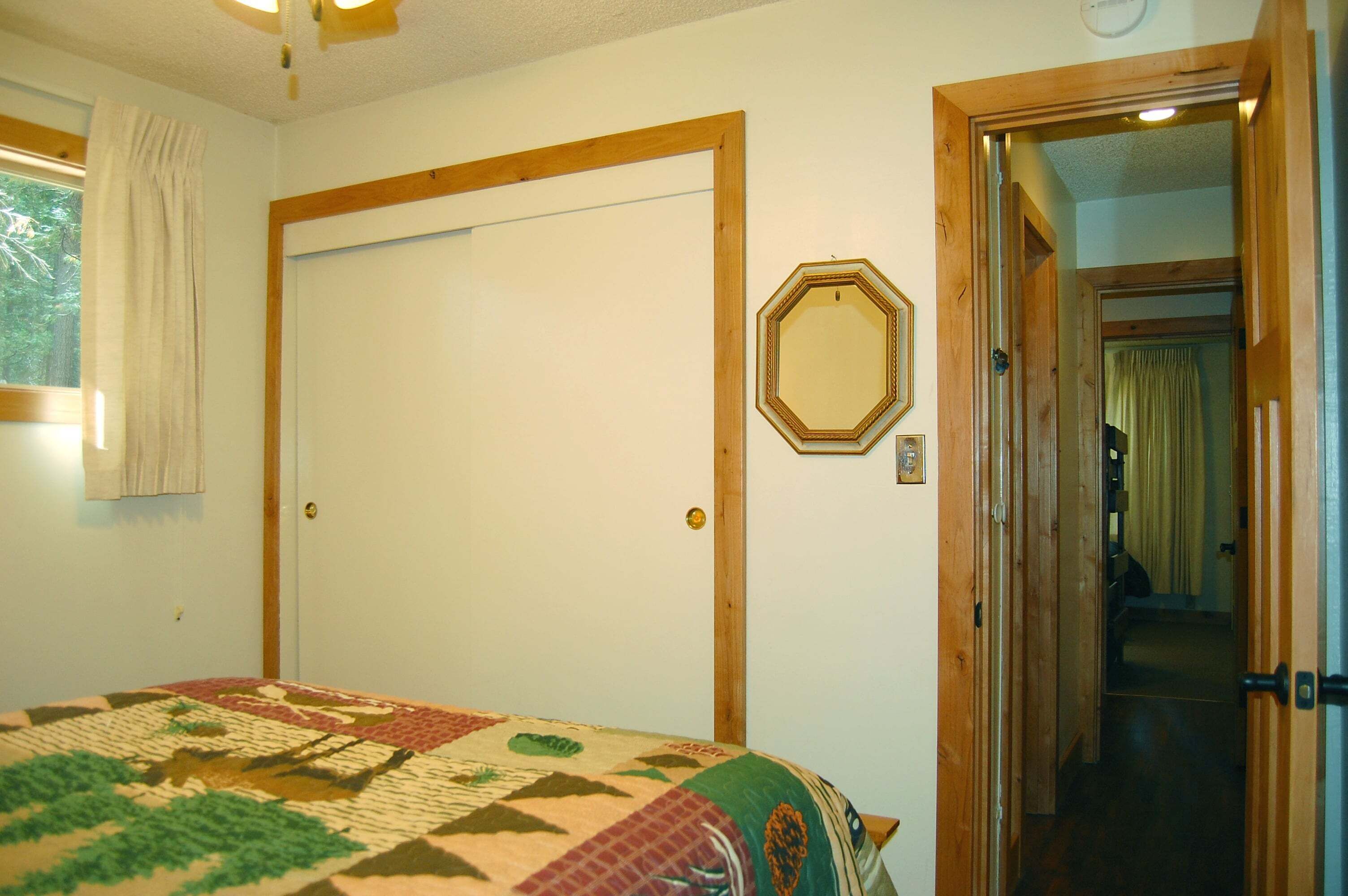 A bedroom with a bed, a door, a mirror, and a window with curtains.