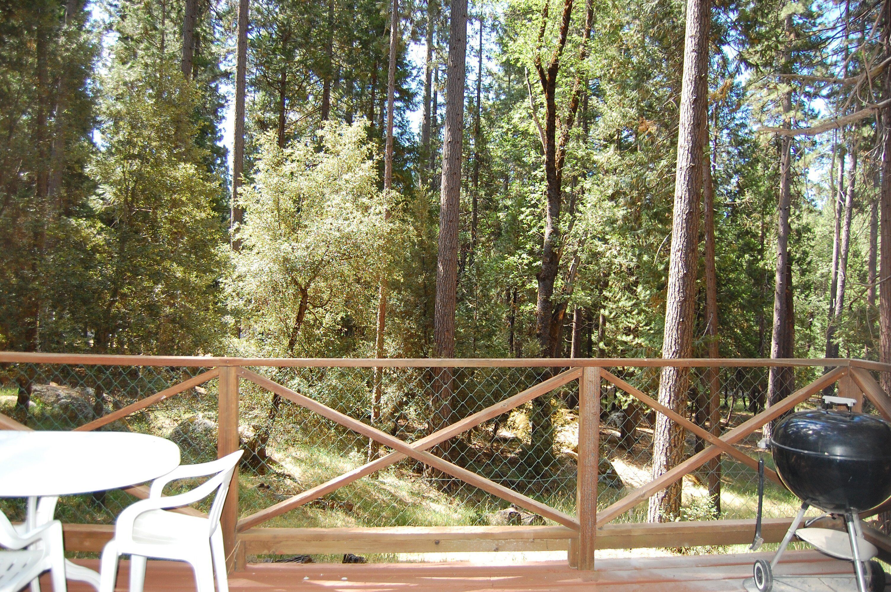 A wooden deck with a chain-link fence, white plastic chairs, and a barbecue grill.