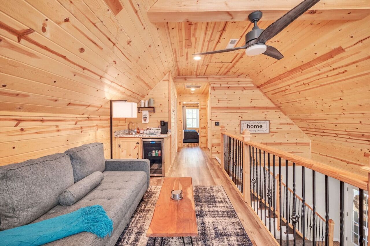 A cozy cabin interior with a wooden interior, a sofa, a coffee table, and a staircase with a railing.