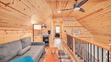 A cozy cabin interior with a wooden interior, a sofa, a coffee table, and a staircase with a railing.