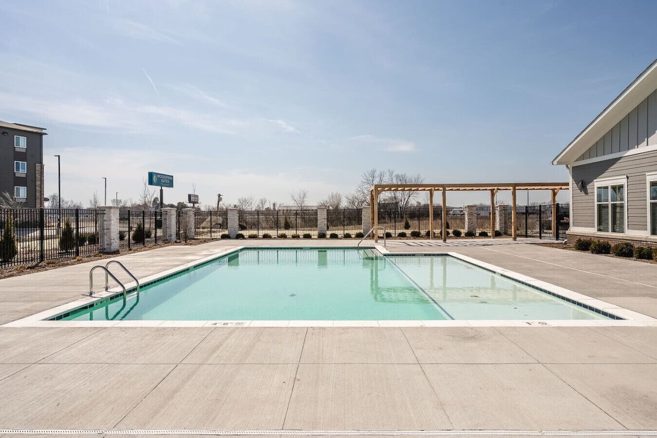 Una piscina rettangolare con una pergola in legno e un'area recintata.