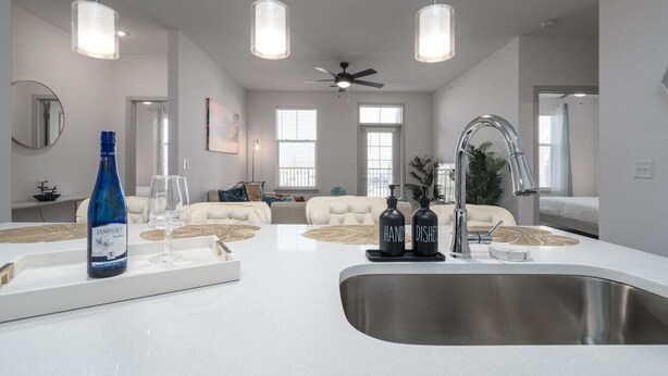 A modern kitchen with a central island, stainless steel sink, pendant lights, and a ceiling fan. - Lovely 2-bedroom-free Parking (Whitestown)