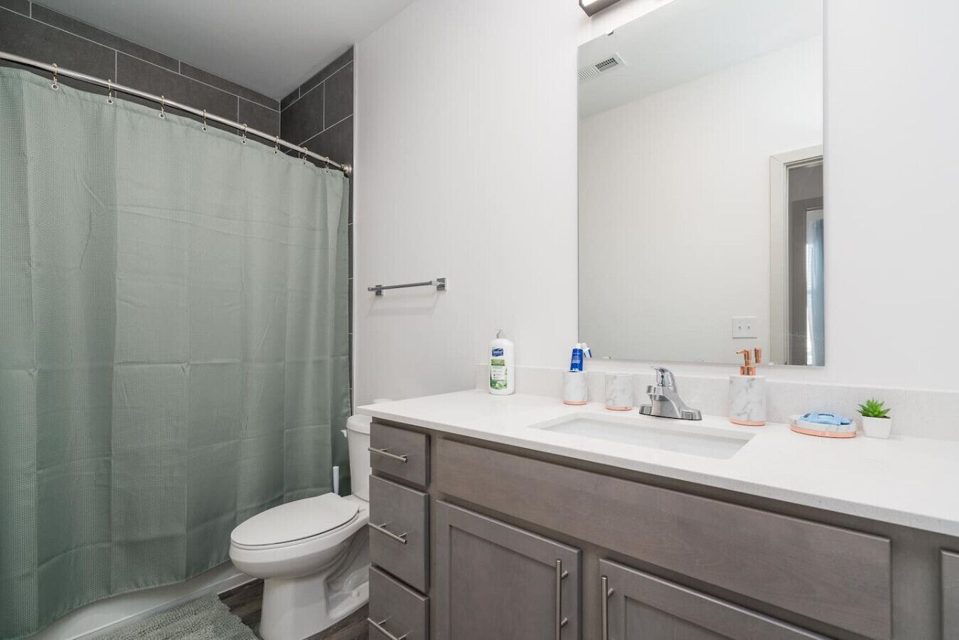 A modern bathroom with a shower curtain, toilet, vanity with a mirror, and toiletries.