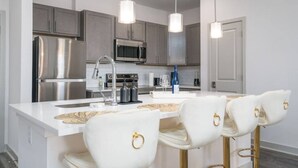 A modern kitchen with stainless steel appliances, white bar stools, and pendant lighting. - Lovely 2-bedroom-free Parking (Whitestown)