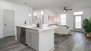A modern kitchen with a central island, stainless steel appliances, pendant lighting, and a dining area with a white sofa and a coffee table. - Lovely 2-bedroom-free Parking (Whitestown)
