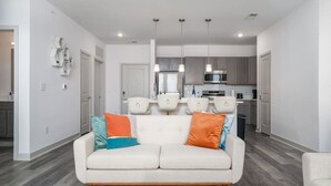A modern living room with a white sofa, colorful cushions, and a kitchen in the background. - Lovely 2-bedroom-free Parking (Whitestown)
