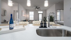 A modern kitchen with a central island, stainless steel sink, pendant lights, and a ceiling fan. - Lovely 2-bedroom-free Parking (Whitestown)