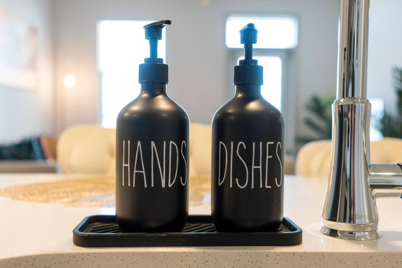 Two black bottles with pumps on a kitchen counter, labeled "HANDS" and "DISHES".