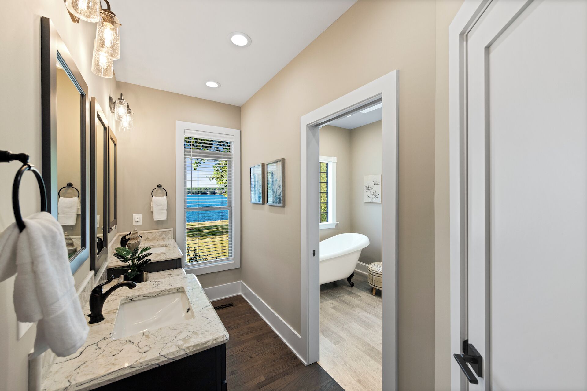 A modern bathroom with a large mirror, two sinks, a bathtub, and a window with a view.