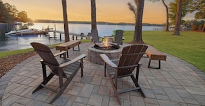 Uma área de estar ao ar livre com cadeiras Adirondack, um braseiro e vista para um lago com barcos.