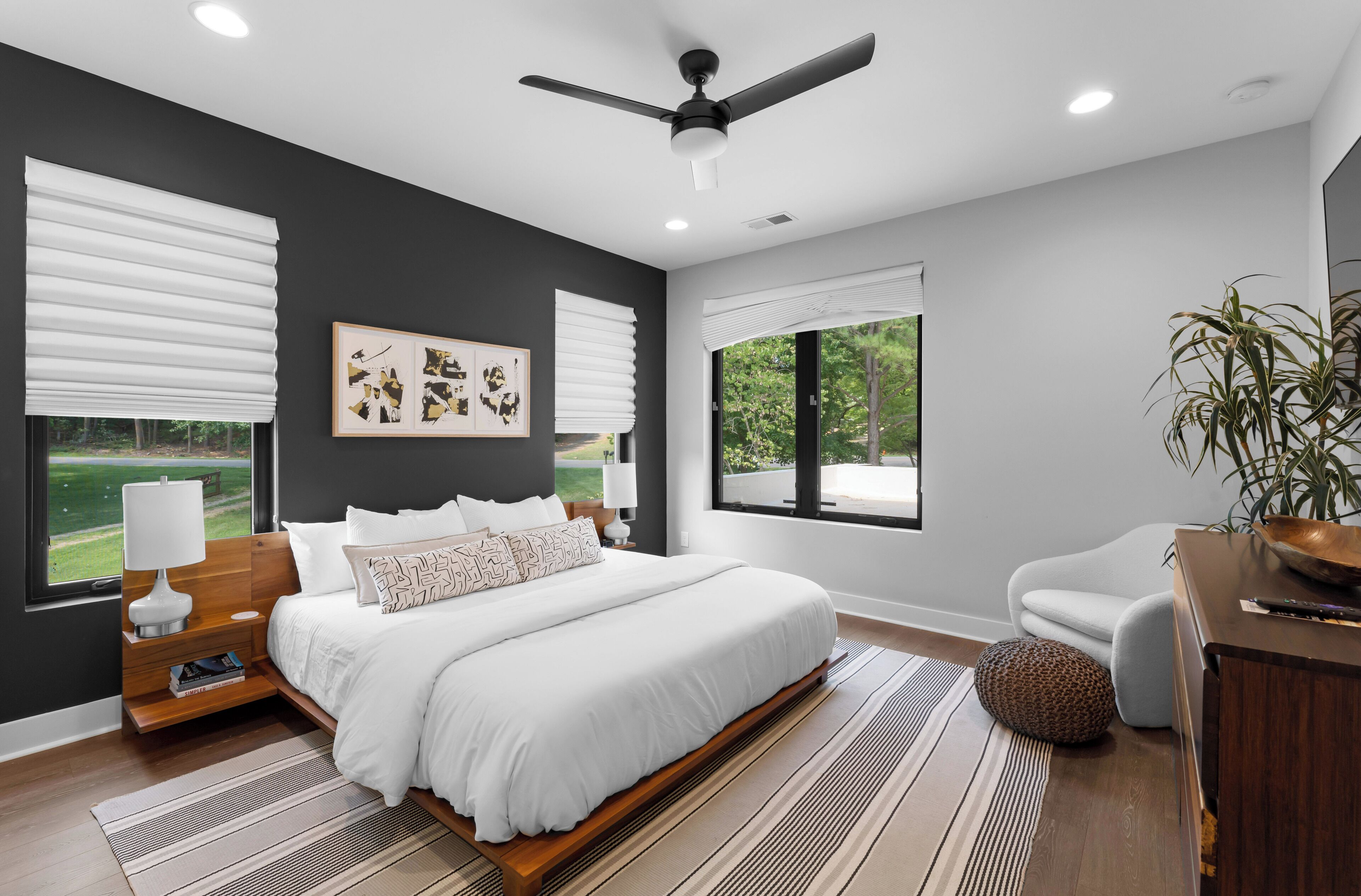 A modern bedroom with a large bed, a ceiling fan, and a view of the outdoors.