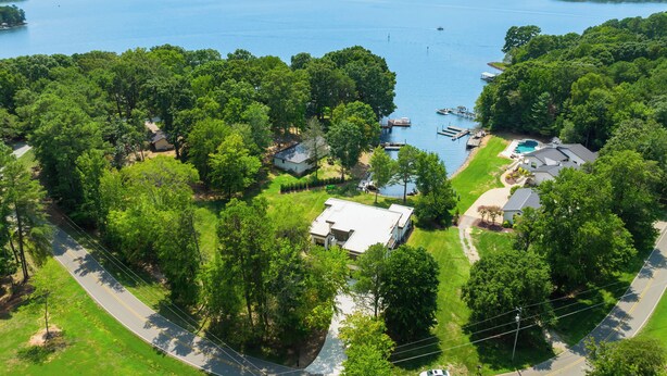 An aerial view of a lakeside property with a dock, swimming pool, and multiple houses surrounded by dense trees. - Shoreline on Stonemarker (Mooresville)