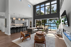 Uma sala de estar ampla com uma grande janela com vista para uma piscina, uma cozinha com eletrodomésticos modernos e um espaço de jantar com banquetas.