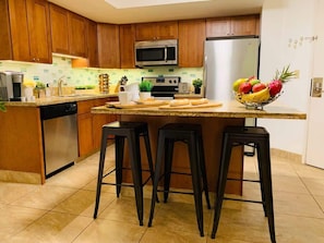 Une cuisine avec des meubles en bois, un four à micro-ondes en acier inoxydable, un réfrigérateur et un panier de fruits posé sur le plan de travail.