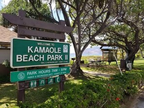 Segnaletica di benvenuto per il Kamaole Beach Park II, con orari di apertura dal 7:00 all'8:00 PM, e un'area picnic con tavoli e panchine.