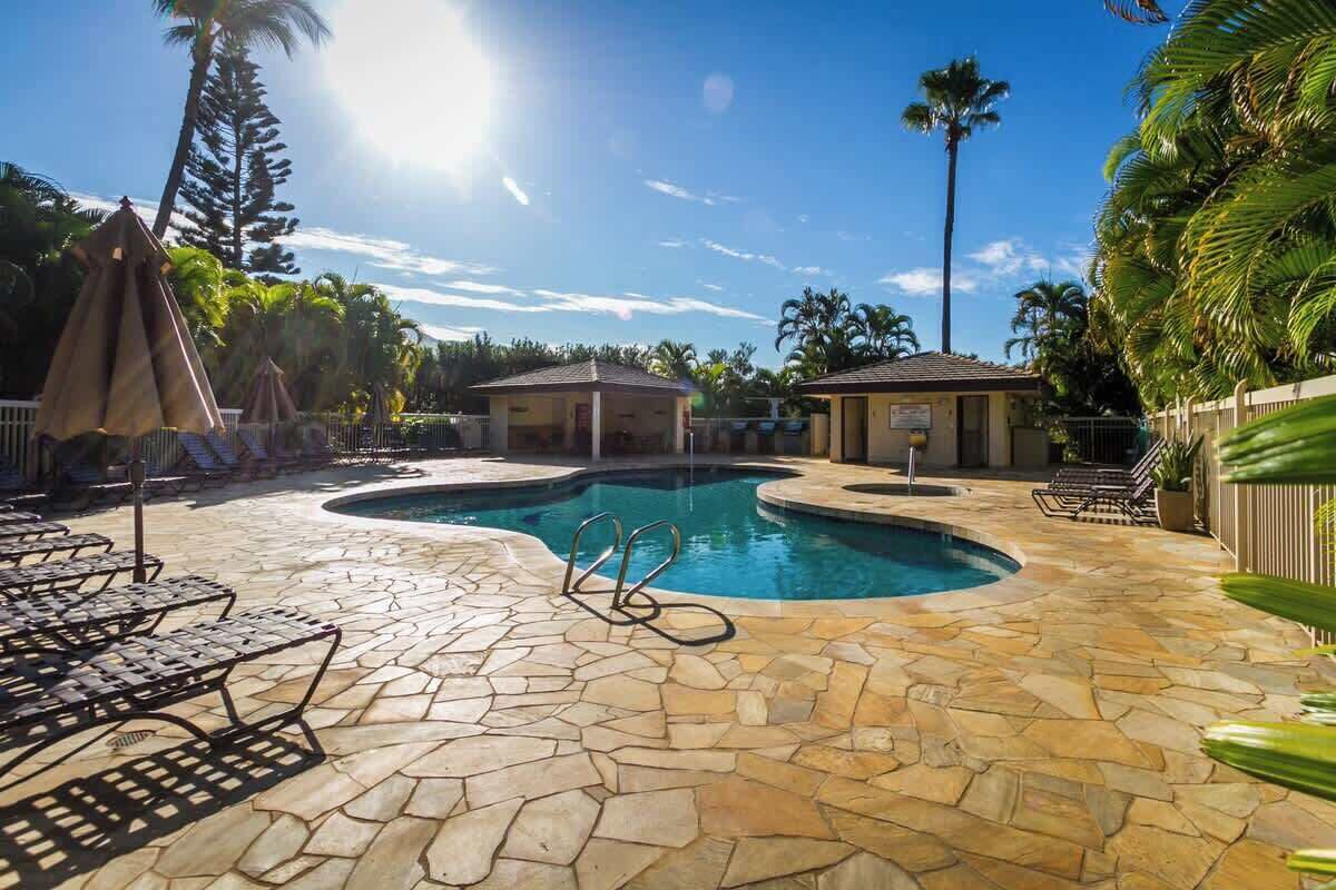 A swimming pool with stone tiles, lounge chairs, and palm trees.