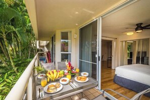 Un balcone con prodotti per la colazione, un letto e vista su piante tropicali.
