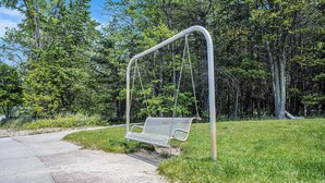 Une balançoire dans un parc, avec un chemin pavé et une zone herbeuse.