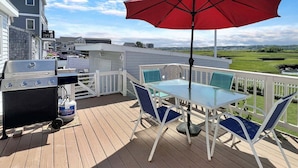 Une terrasse avec un barbecue, une table avec des chaises et un parasol rouge.