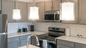 A modern kitchen with stainless steel appliances, grey cabinets, and pendant lighting. - Luxurious One Bedroom Whitestown (Whitestown)