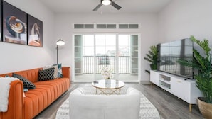 A modern living room with a sofa, coffee table, TV, and balcony doors. - Luxurious One Bedroom Whitestown (Whitestown)