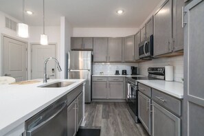 A modern kitchen with stainless steel appliances, grey cabinetry, and a white countertop. - Luxurious One Bedroom Whitestown (Whitestown)