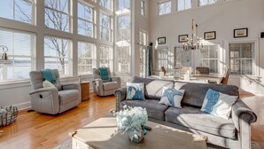 A spacious living room with large windows, a gray sofa, and a coffee table with decorative items. - Eagle Roost Chalet- Modern Kentucky Lake Chalet (Waverly)