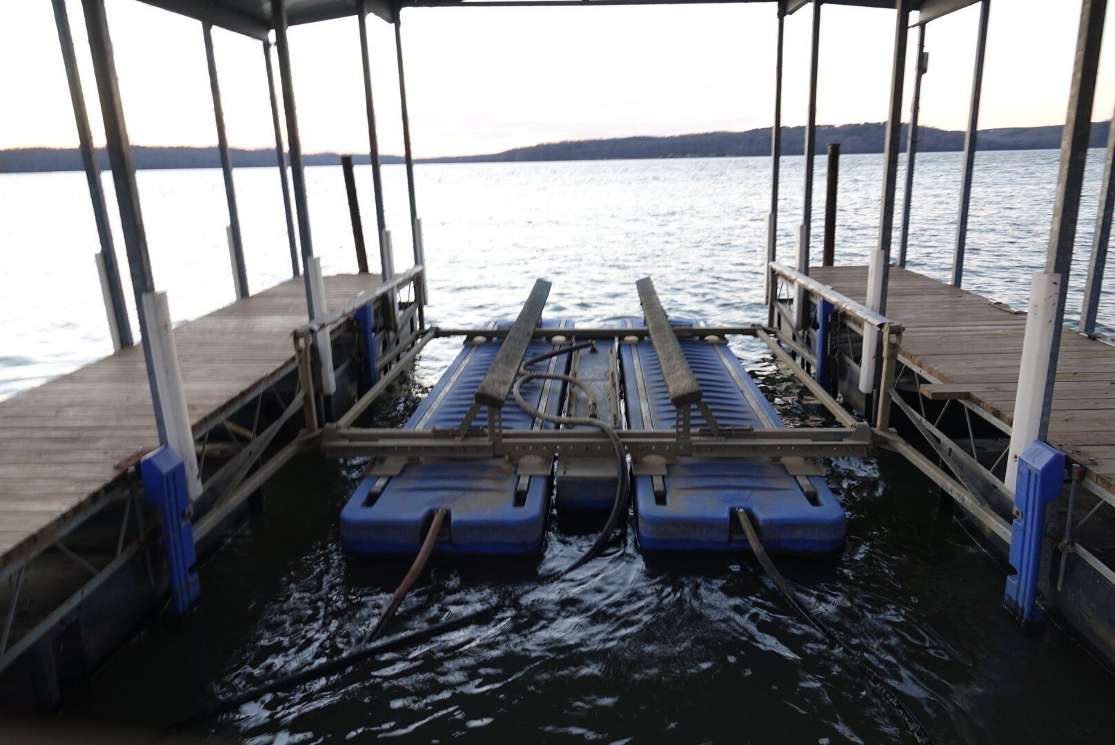 A pier with a wooden deck and metal railings, extending over calm water with a distant shoreline.